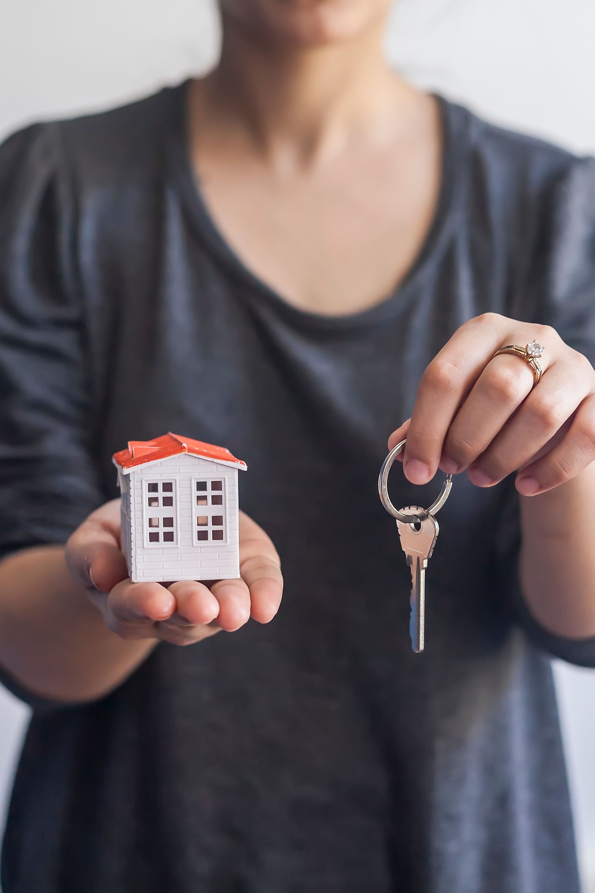 Woman holding miniature toy house and keys. Real estate agent holding keys and toy house. Buying or selling real estate